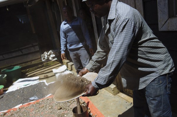 A mineral trader (negociant) filters cassiterite ore in the yard of his home
